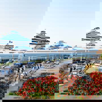 Poolside terrace with striped sun loungers, matching umbrellas, colorful flowers and sea view