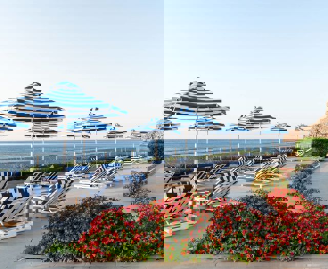 Poolside terrace with striped sun loungers, matching umbrellas, colorful flowers and sea view