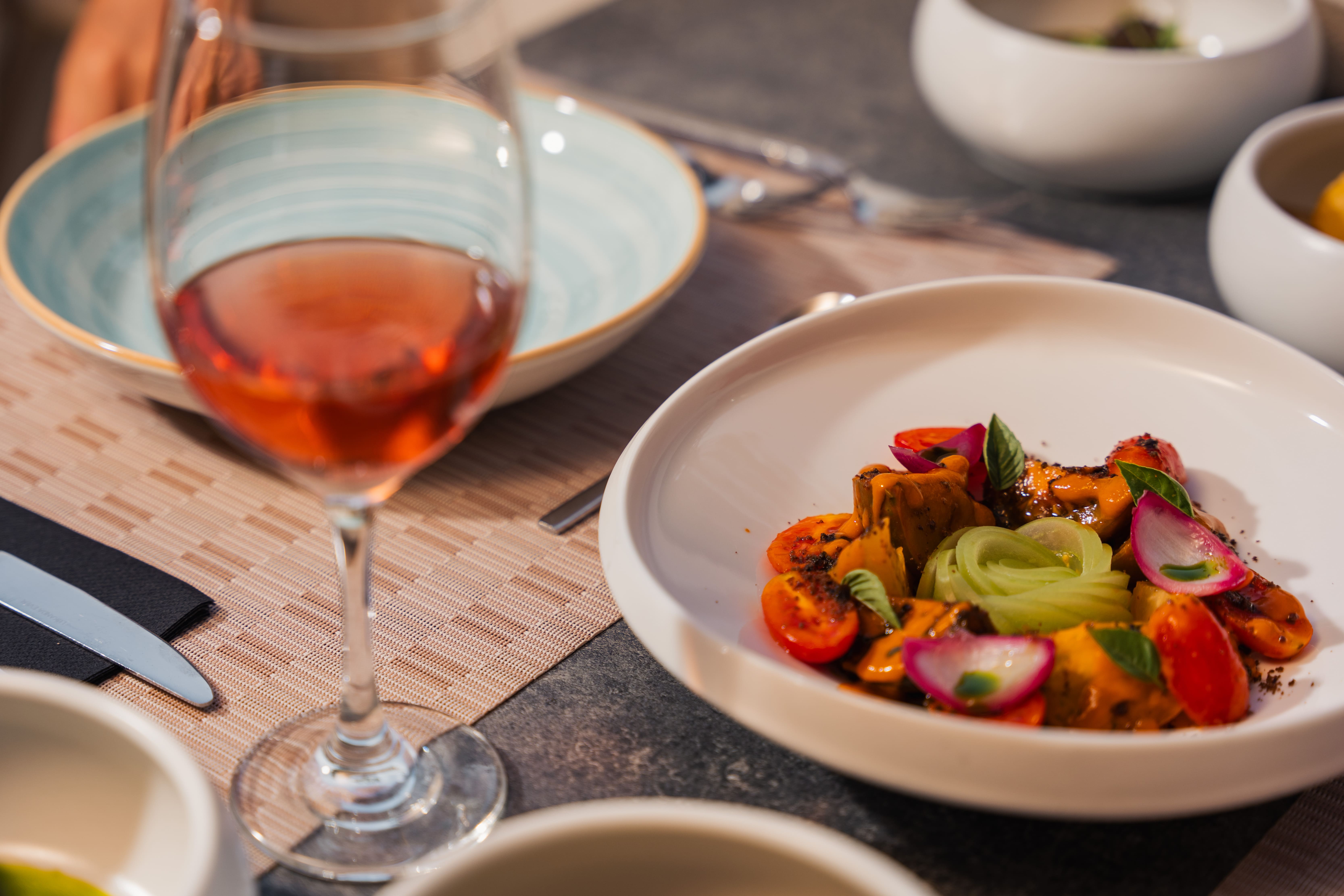 Glass of rosé beside a salad of cherry tomatoes, cucumber ribbons, radish and basil, with a turquoise swirl plate