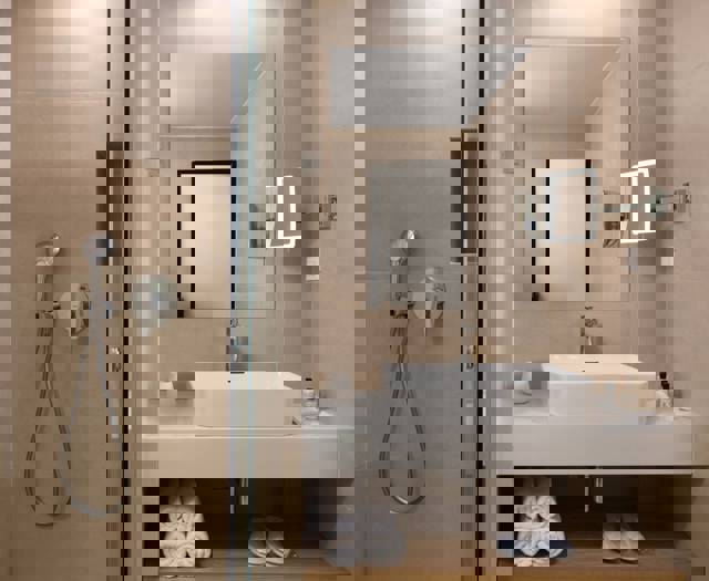 Modern bathroom with walk-in shower, rectangular sink, large mirror and rolled towels on shelf
