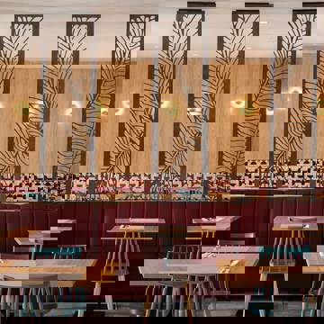 Restaurant interior with wooden tables, red upholstered seating, patterned tile wall and decorative dividers