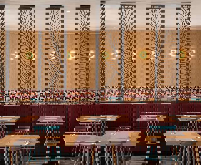 Restaurant interior with wooden tables, red upholstered seating, patterned tile wall and decorative dividers