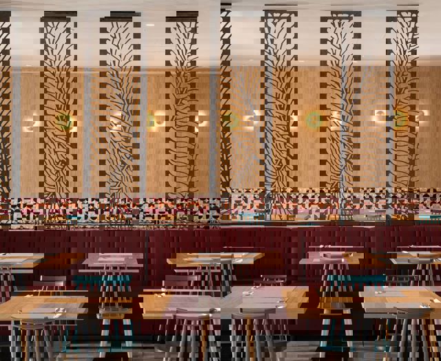 Restaurant interior with wooden tables, red upholstered seating, patterned tile wall and decorative dividers
