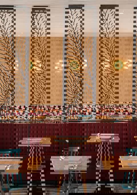 Restaurant interior with wooden tables, red upholstered seating, patterned tile wall and decorative dividers