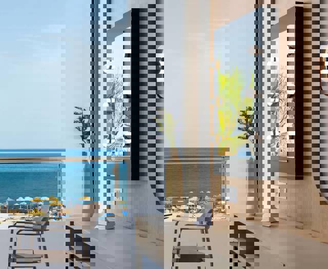 Premium Deluxe hotel room's desk with mirror and chair, balcony view of beach umbrellas, palm trees and the sea