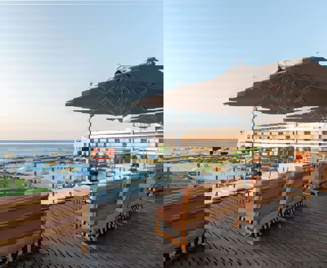 Outdoor sitting area with wooden benches, large umbrellas and view of pool, sun loungers and sea