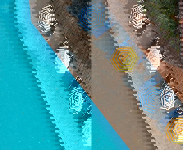 Aerial view of poolside loungers with striped umbrellas next to a swimming pool