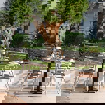 Outdoor dining table with four white chairs set near a garden with a large tree