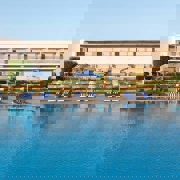 Swimming pool with blue loungers, striped umbrellas and hotel building in the background