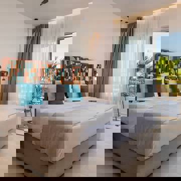 Premium Deluxe hotel room with large bed, patterned headboard, balcony and sea view through glass doors