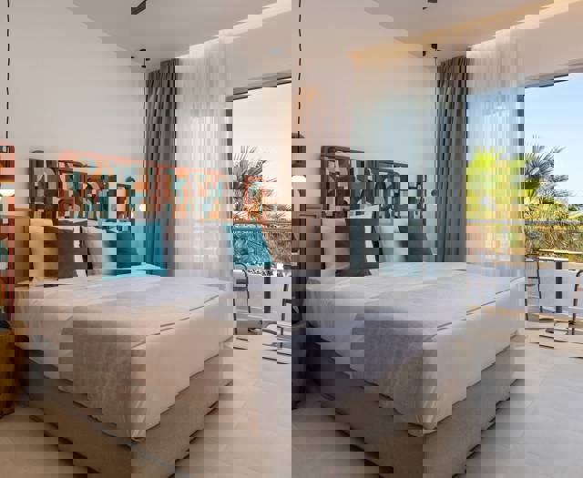 Premium Deluxe hotel room with large bed, patterned headboard, balcony and sea view through glass doors