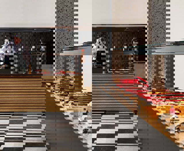 Buffet station with red serving trays, baskets of bread and chef preparing food behind striped counter