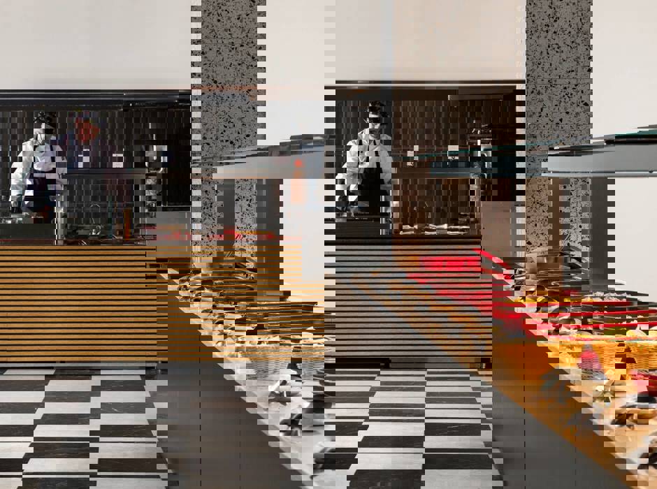 Buffet station with red serving trays, baskets of bread and chef preparing food behind striped counter